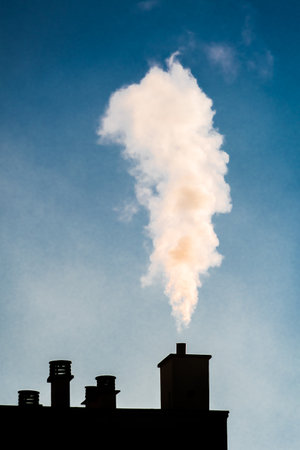White smoke coming out of a chimney on the roof of a residential building. Concepts of cold, heating, and pollutionの写真素材