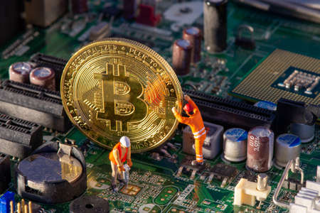 Bitcoin mining inside a computer. Two small Bitcoin miners figurines extracting valuable electronically-mined digital cryptocurrency from motherboard circuitsの写真素材
