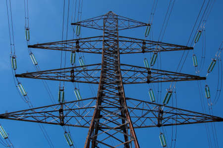 Metal pylon with triangles carrying overhead electric cables of high voltage lines. Concepts of electric transmission grids, energy supply and power consumption issuesの写真素材