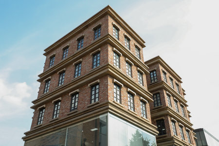 Brick facade of a modern building against a blue sky with cloudsの写真素材