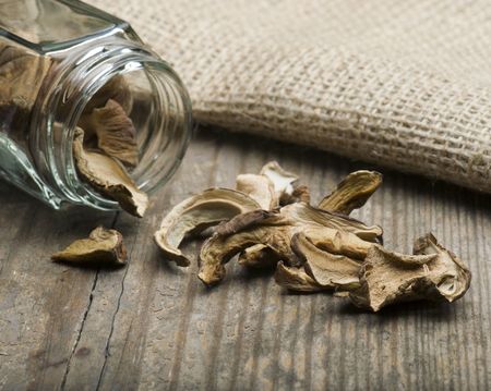 Dried Porcini Mushrooms Spilling Out Of A Jar On To A Wooden Table With A Hessian Bag in The Backgroundの写真素材