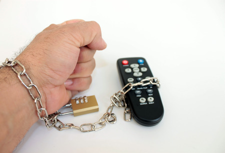 Remote control dependency concept. Male hand tied to the remote with the chain.
