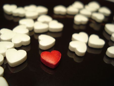 Close-up of a red heart-shaped tablet among the white ones on the dark glossy surface               ...