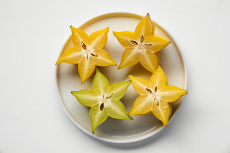 Star fruit slices display their distinctive star shape and bright yellow and green colors on a white plate offering a healthy and visually appealing tropical treat.の写真素材