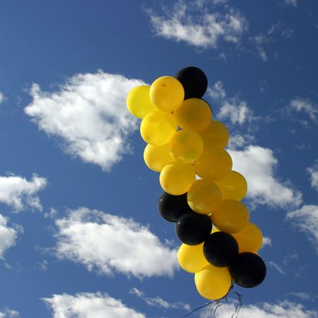 Yellow and black ballons with a blue cloudy skyの写真素材