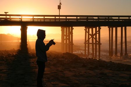 Photographer at sunset sunrise near the pier by the beach and ocean.
