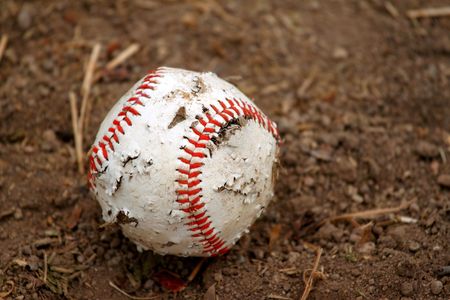 Old red and white rugged baseball on a dirt groundの写真素材