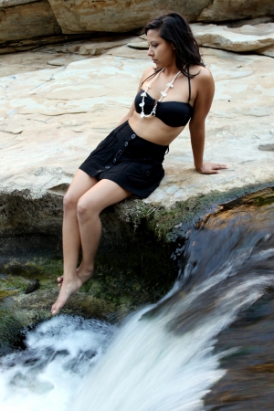 Hispanic woman with bikini sitting next to a waterfall の写真素材