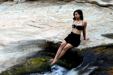 Hispanic woman with bikini lying next to a waterfall.の写真素材