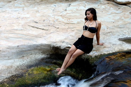 Hispanic woman with bikini sitting next to a waterfall.の写真素材