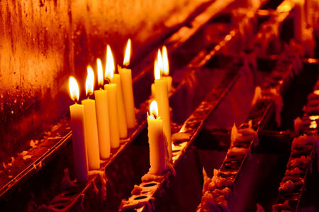 Some candles burning on candle holders in a chapel, causing an atmospheric red glow.の写真素材