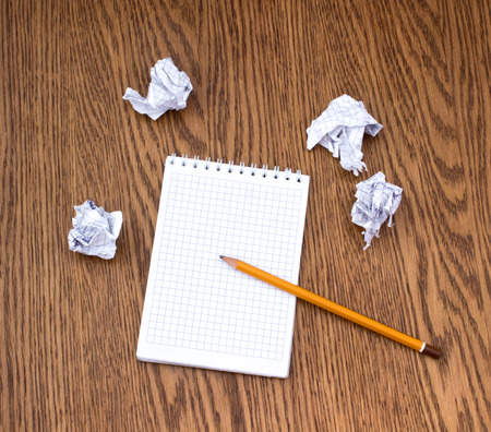 Pencil, clean notebook and several crumpled sheets of paper lying on the wooden tableの写真素材