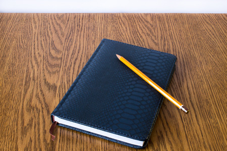 Simple blue leather note with brown bookmark and pencil lies on a wooden table