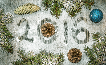 Background for holiday  greeting card. Caption twenty sixteen made for Happy New Year and Merry Christmas on the frozen snow-covered wooden table with cristmas toys and conesの写真素材