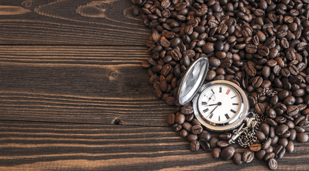 Old pocket watch lying on the coffee beans scattered on the old wooden table. Focus on dialの写真素材