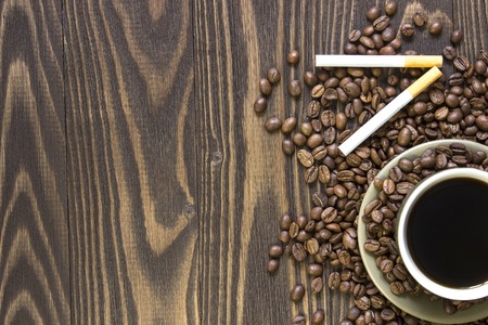 Cup of coffee  with beans, and two cigarettes  standing on a wooden table. Crop. Top viewの写真素材