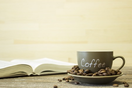 A cup of coffee with beans on the background of a  book. Focus on the edge of the cupの写真素材