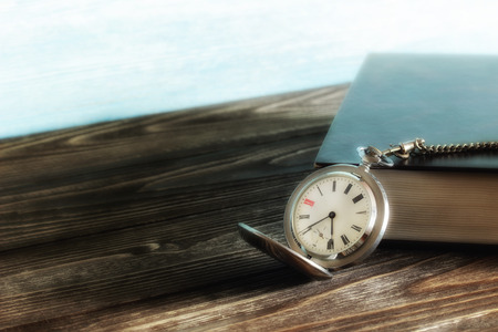 Old vintage silver pocket watch and book with black cover on wooden table. Blurred. Soft focusの写真素材