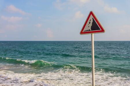 Warning sign rockfall at the steep coast with ocean and cloudy skyの写真素材