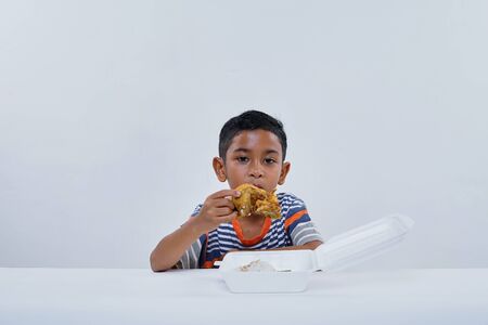 Schoolboy eating fried chicken fastfood on white backgroundの写真素材