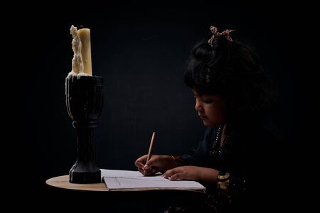 Cute little girl studying under illuminated candle lightの写真素材