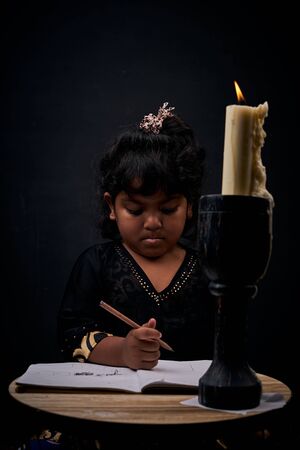 Cute little girl studying under illuminated candle lightの写真素材