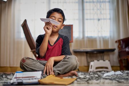 Cute kid boy playing handmade paper airplane at home