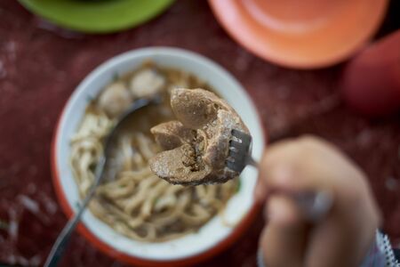 Customer eating Meatballs and Noodles soup and vegetable at street food market. Traditional delicious Indonesian foodの写真素材