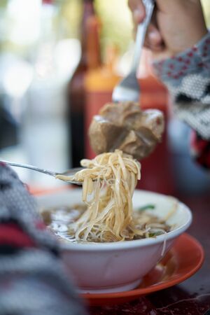 Customer eating Meatballs and Noodles soup and vegetable at street food market. Traditional delicious Indonesian foodの写真素材