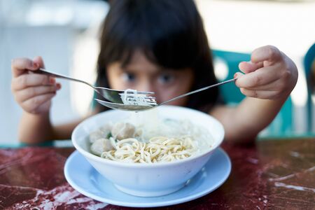 Little Girls eating chinese noodle with meatballs at street food marketの写真素材
