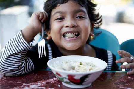 little Asian girl eating ramen noodles at Japanese restaurantの写真素材