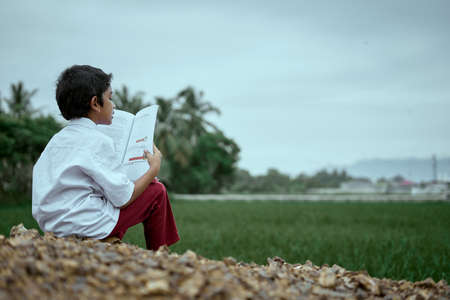 Asian boy wearing school uniform reading and studying outdoor at rice fieldの写真素材