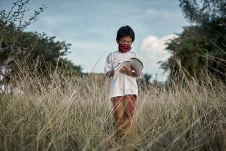 Boy standing wearing protective Face mask reading a book in a meadow natural park. New Normal education and learning conceptの写真素材