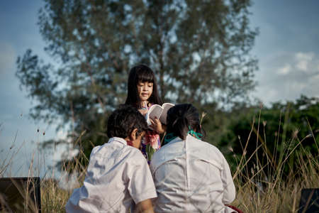 Happy little girl writing a book while her brother and sister doing homework outdoors in the field,...