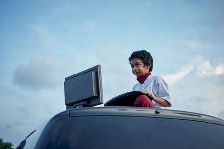 Boy in school uniform playing internet games on top of car roof, New Normal Education conceptの写真素材