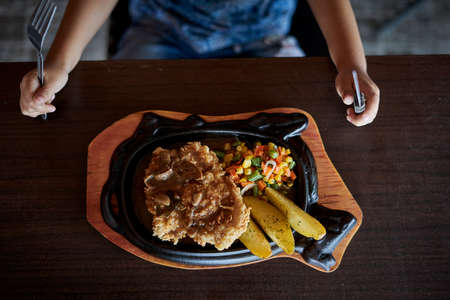 Hands cut a chicken crispy steak on hot plate with barbecue sauce, rice and potatoesの写真素材