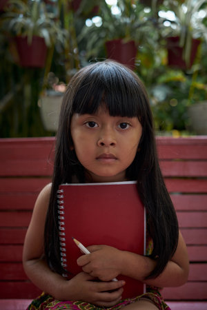 Pretty little girl holding a book and pencil and sitting in the backyardの写真素材