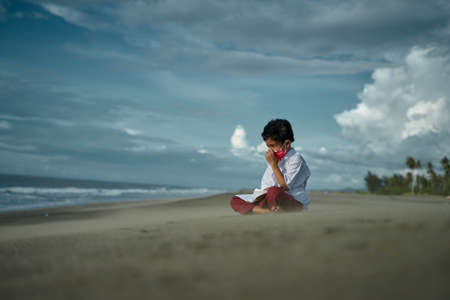 Schoolboy in medical mask reading a book on the beachの写真素材
