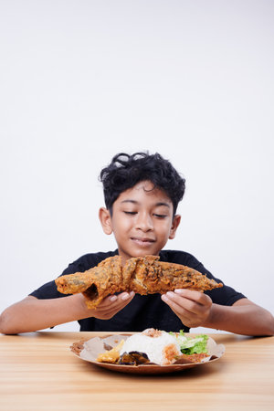 Asian boy enjoys fried fish and rice at lunch timeの写真素材