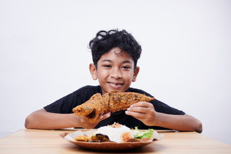 Asian boy enjoys fried fish and rice at lunch time