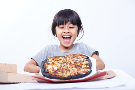 Little asian girl eating pizza isolated on white background. Studio shot.の写真素材