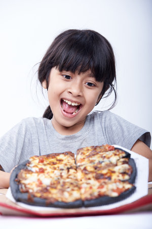 Little asian girl eating pizza on white background. Studio shot.の写真素材