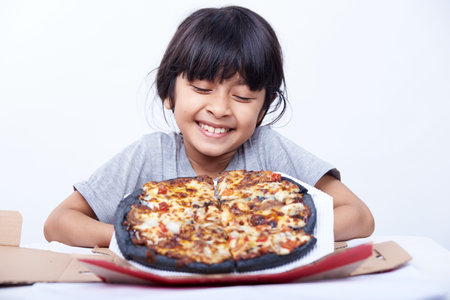 Asian Chinese little girl eating pizza in a box on a white backgroundの写真素材