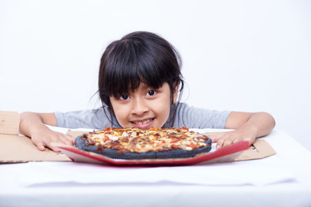 Little Asian girl eating pizza on the table isolated on white background.の写真素材