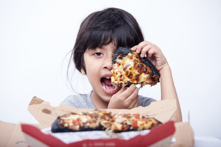Asian little girl eating pizza in a box on white background.の写真素材