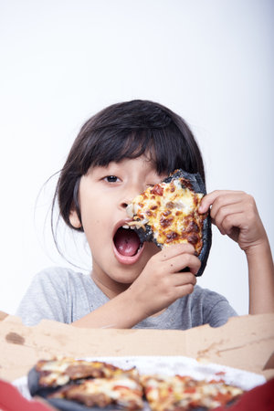 Little asian girl eating pizza isolated on white background, studio shotの写真素材