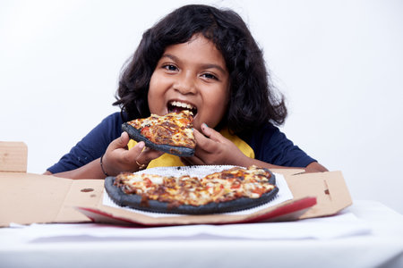 Indian little girl eating pizza at home, isolated on white background.の写真素材