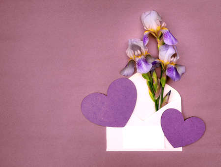 Card with a bouquet of irises in an envelope with hearts on a pink background. Top view with copy space.の写真素材