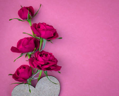 Bright red pink roses with a heart on a pink background. Postcard with place for design. Flower composition.の写真素材