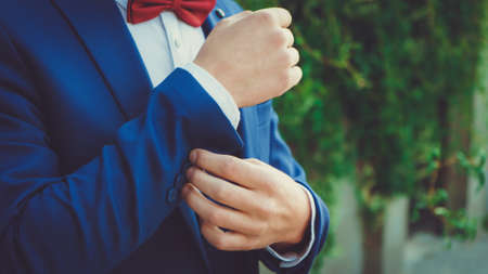 Hands of a young man in a blue suit with a red bow tie close up